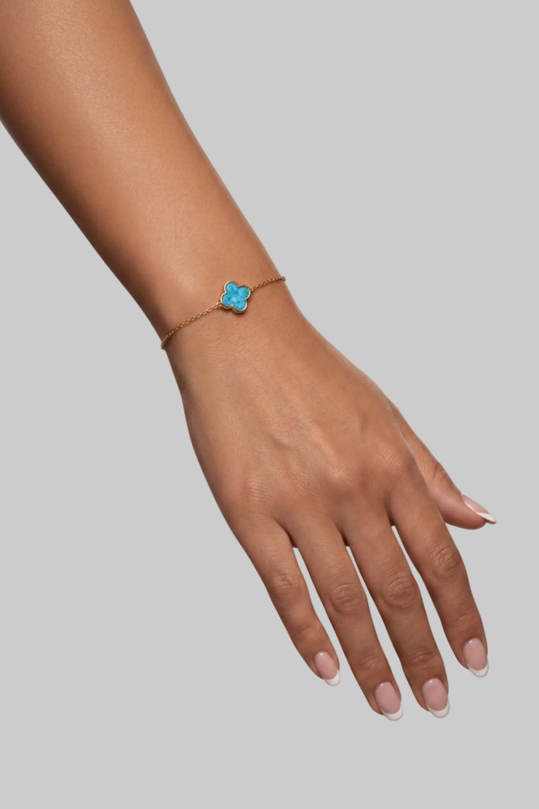 Gold bracelet on wrist with blue four-leaf clover charm
