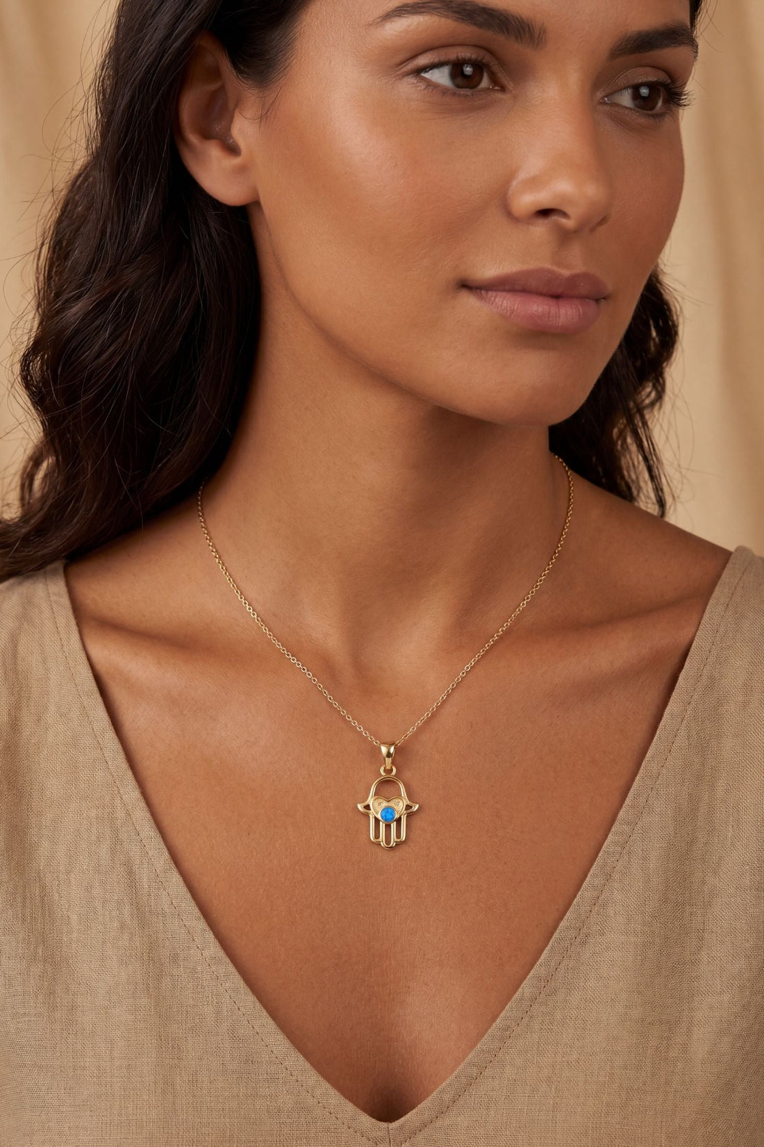 Gold hamsa hand pendant necklace with blue opal-style center, worn at neckline