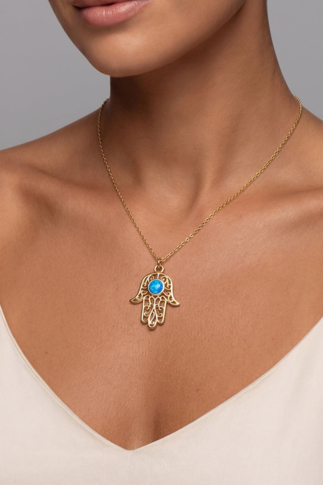 Gold hamsa pendant necklace worn on neck with blue opal-style center stone
