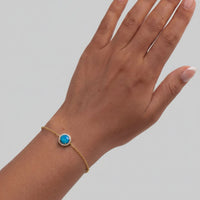 Gold-tone round blue opal bracelet on wrist with small blue bezel stones