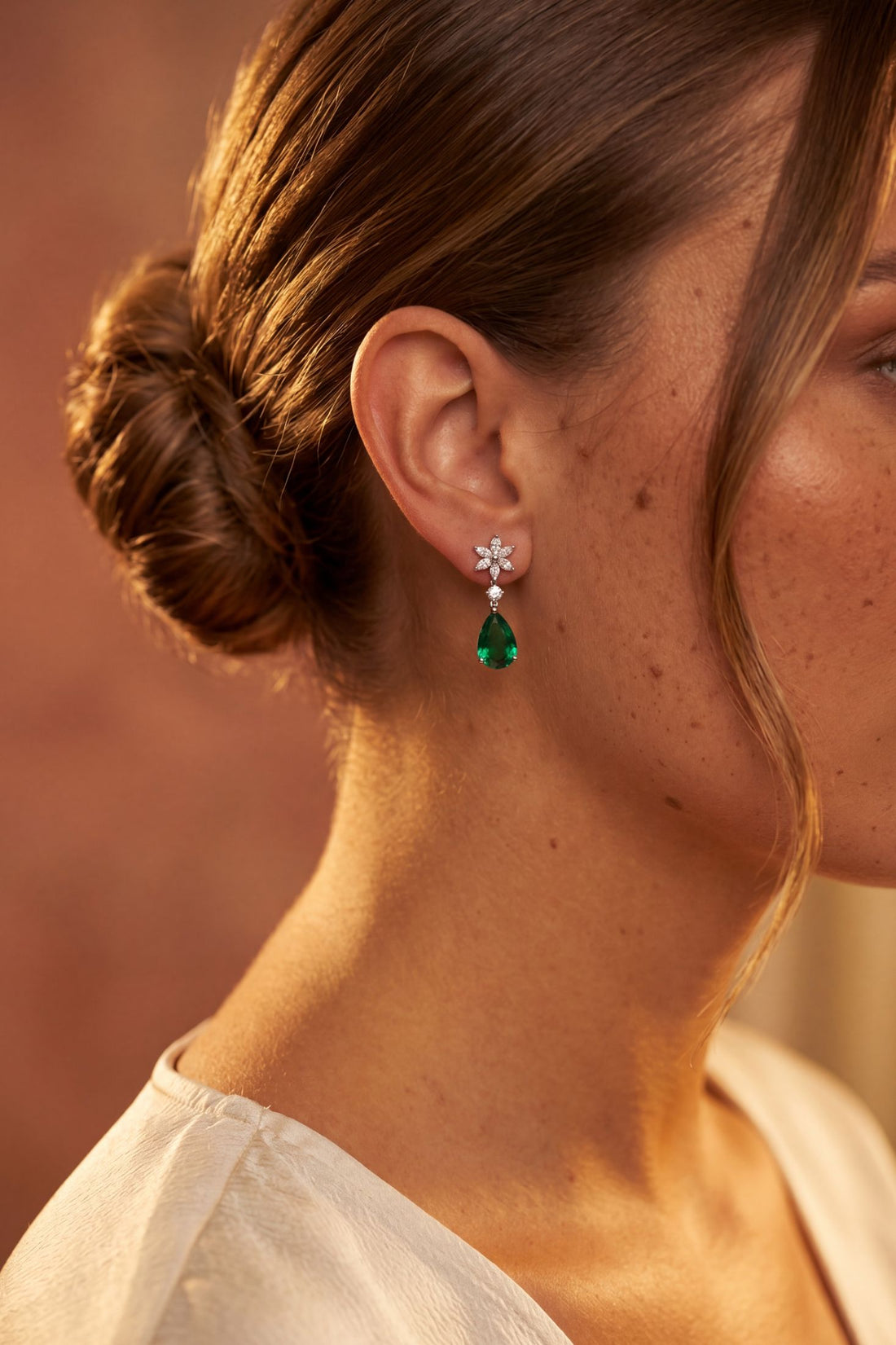 Silver crystal dangle earrings with emerald-green teardrop stones on ear