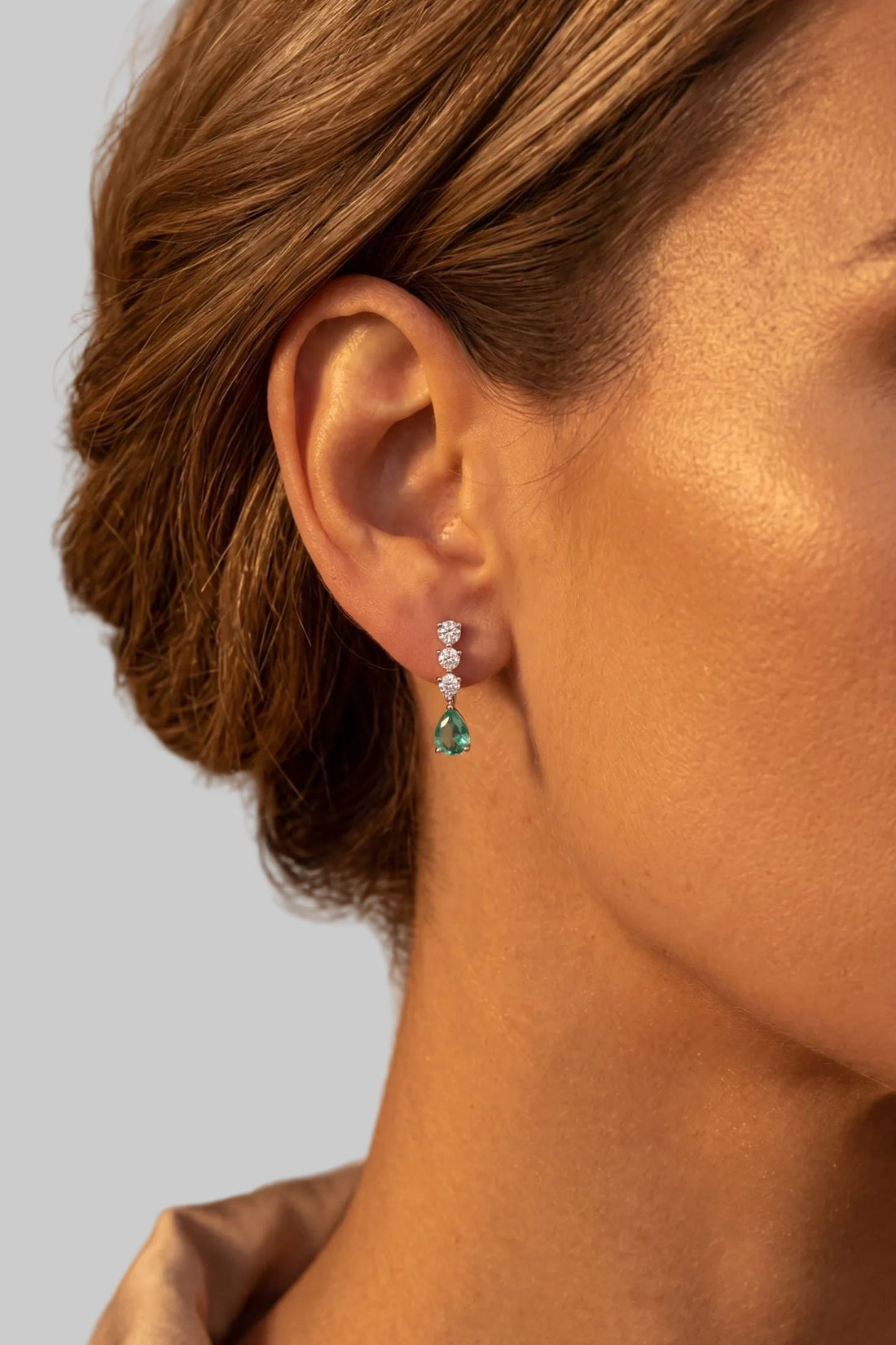 Silver drop earrings on ear with teal pear-shaped stone and small sparkle cluster
