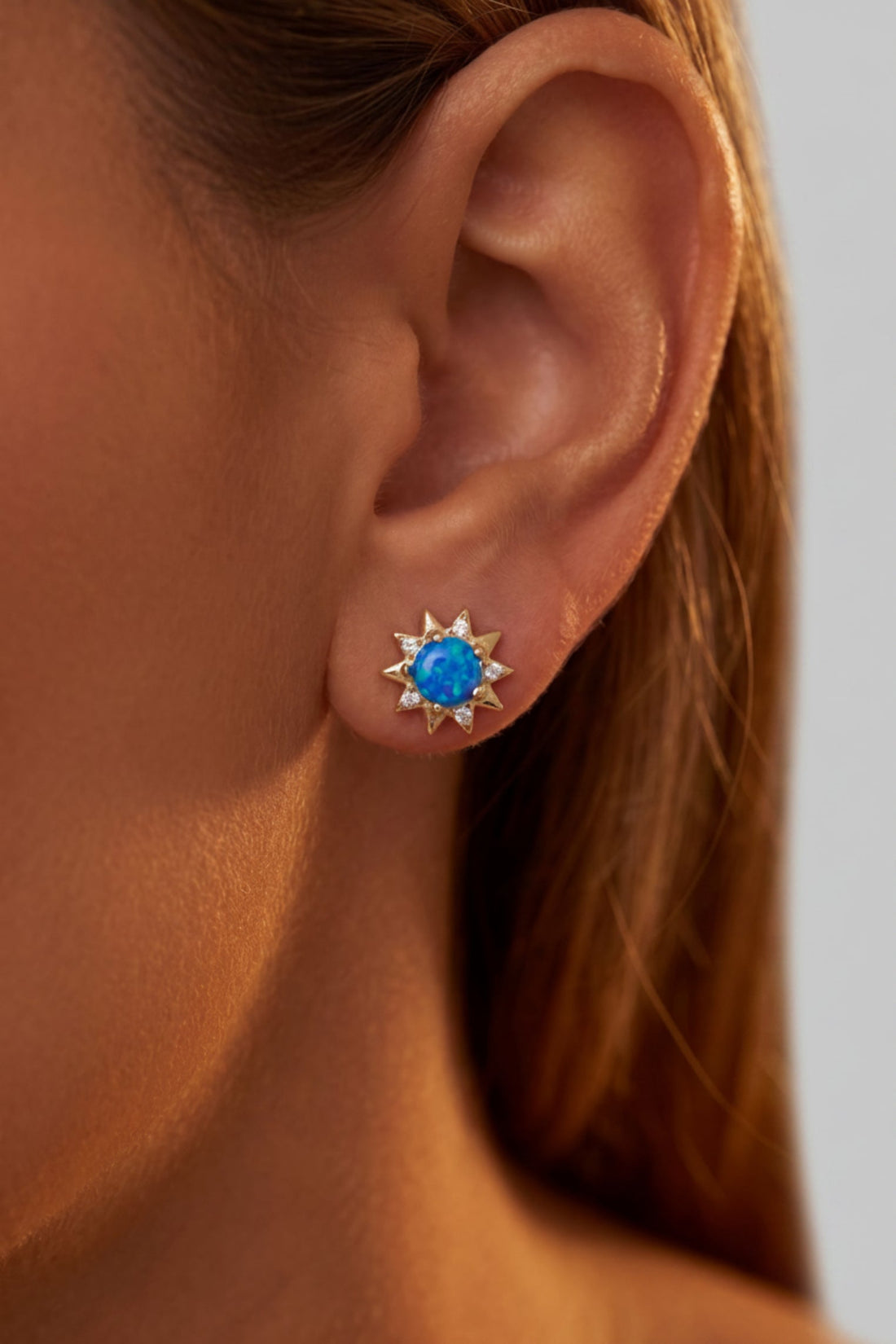 Gold sunflower blue opal stud earrings on ear with clear crystal accents
