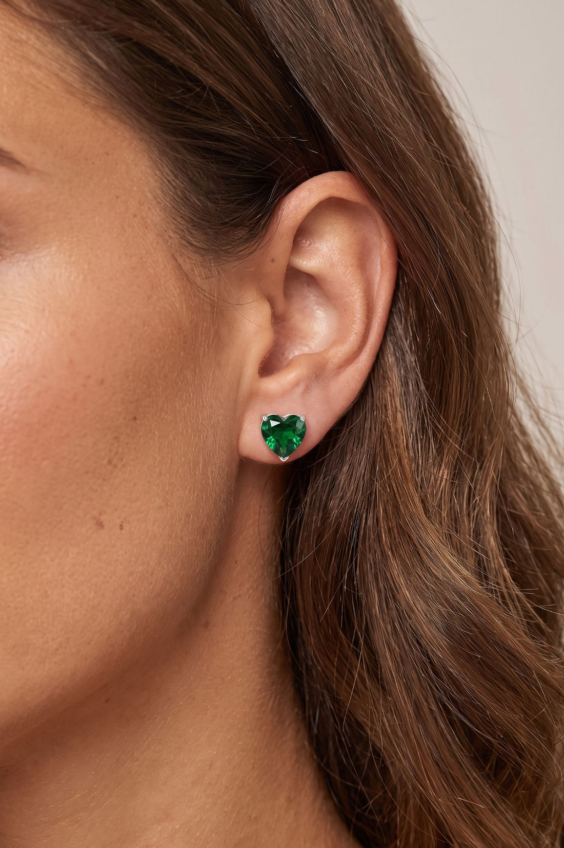 Silver heart stud earrings with emerald-green gemstone on ear