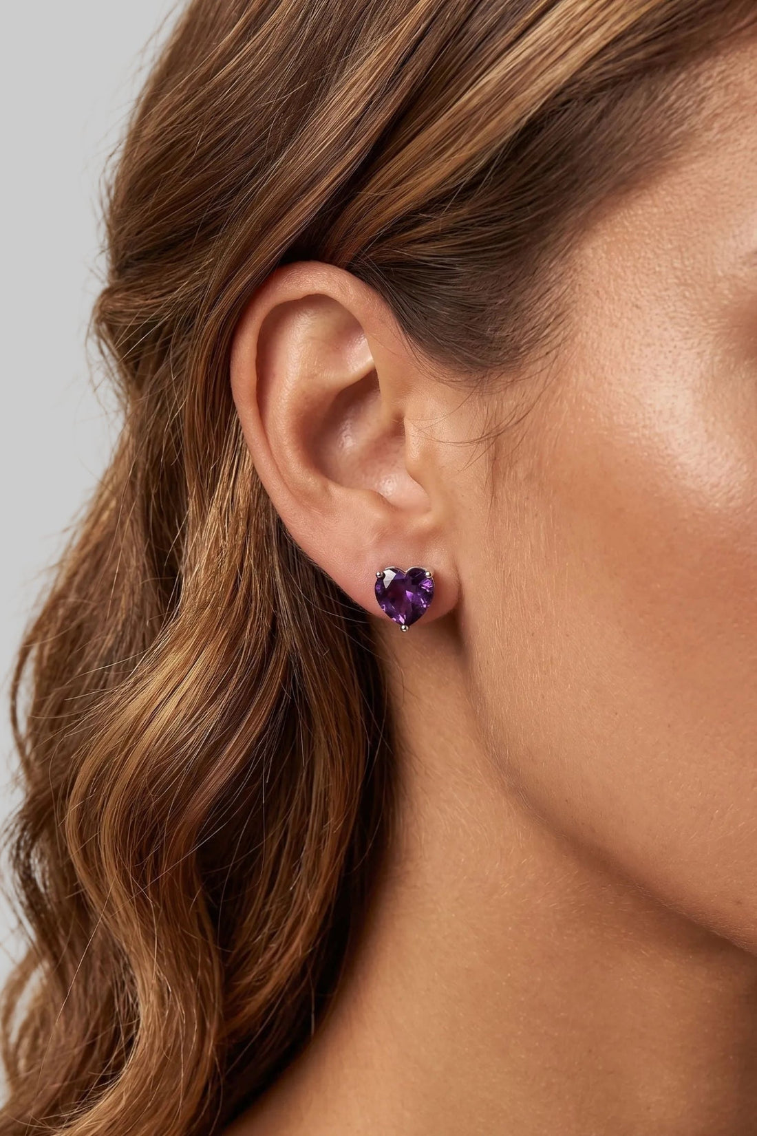 Heart-shaped amethyst stud earrings with purple stones on silver posts, worn