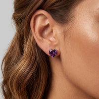 Heart-shaped amethyst stud earrings with purple stones on silver posts, worn