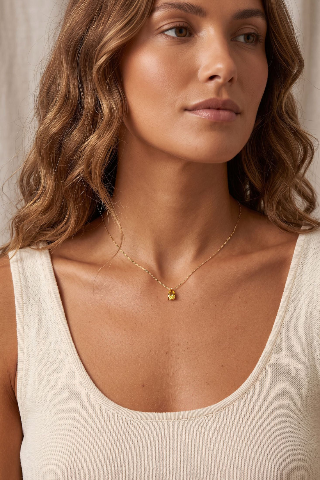 Gold teardrop necklace with small yellow citrine pendant worn on a chain