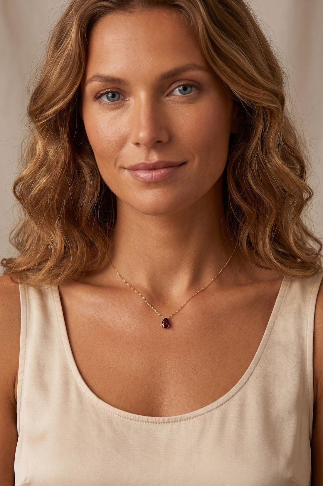 Gold chain necklace with small red teardrop gem pendant
