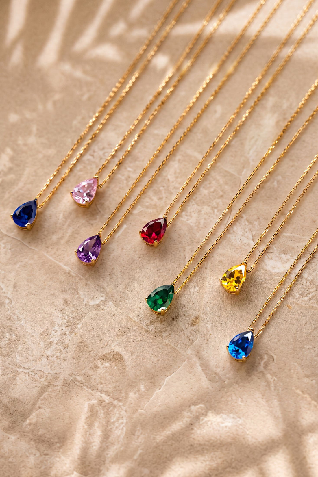 Gold teardrop gemstone pendants on chains with blue, green, red, and yellow stones