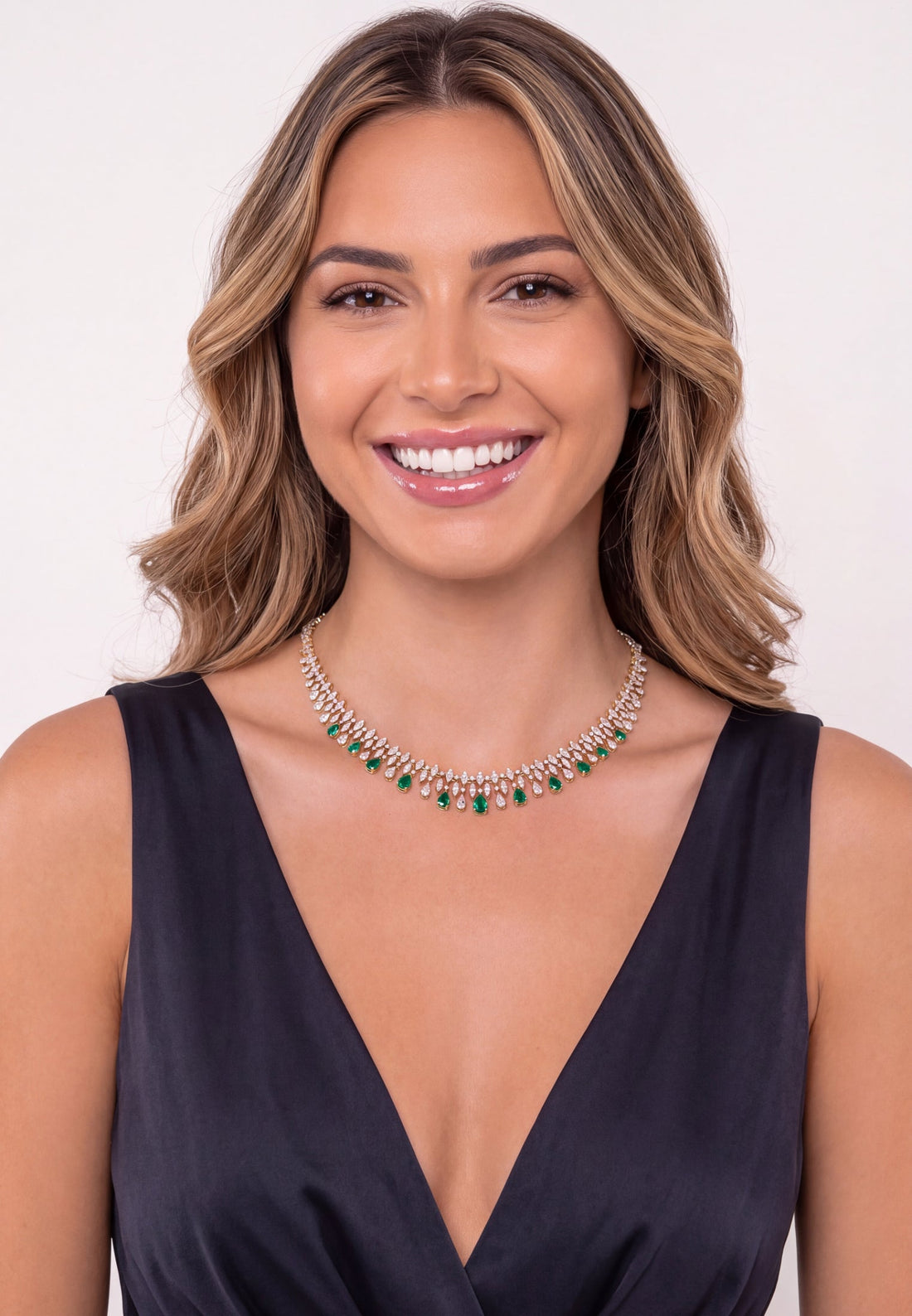 Gold necklace with emerald teardrop stones, worn at V-neckline