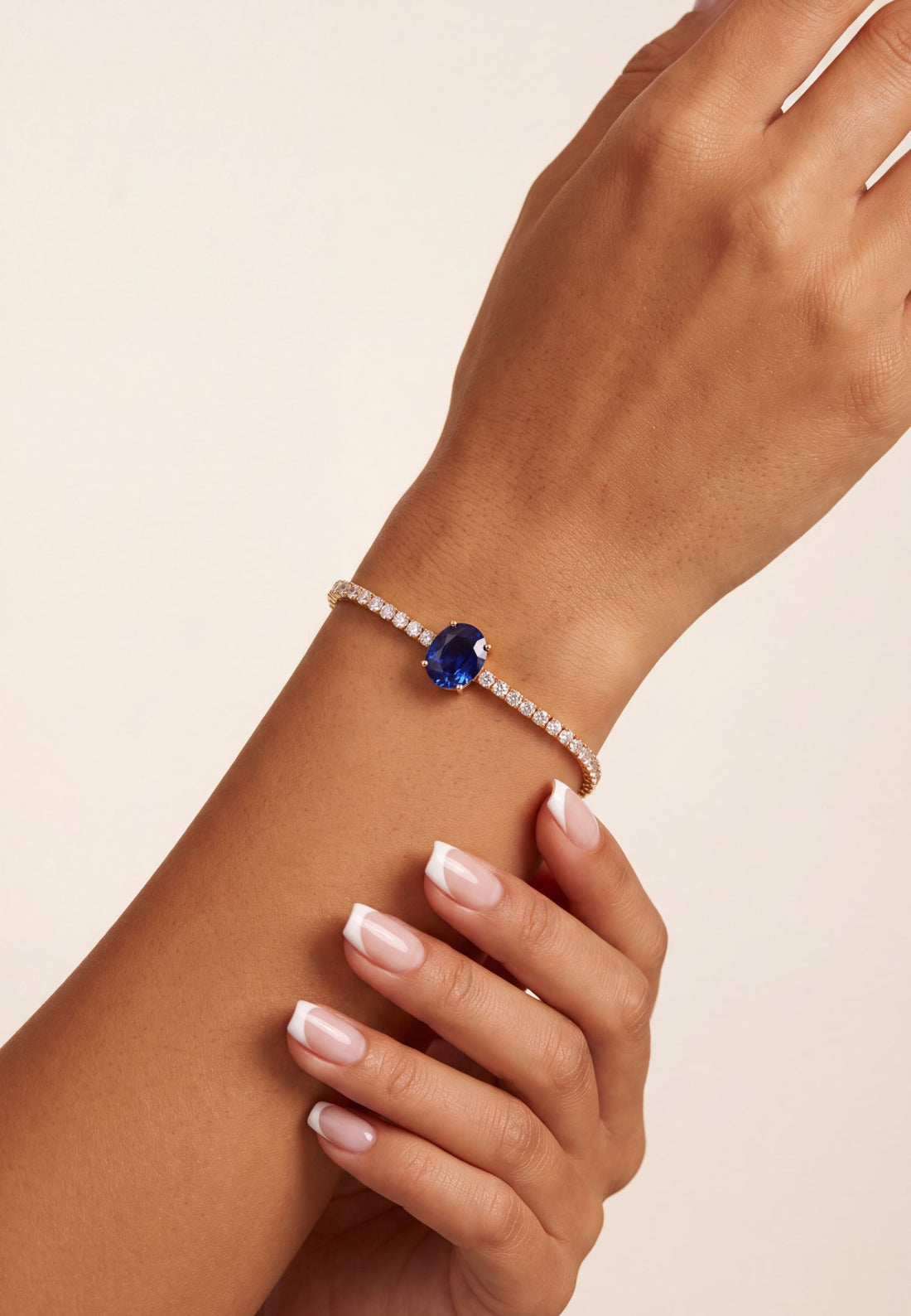 Gold tennis bracelet with oval sapphire centerpiece on wrist