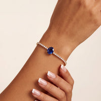 Gold tennis bracelet with oval sapphire centerpiece on wrist