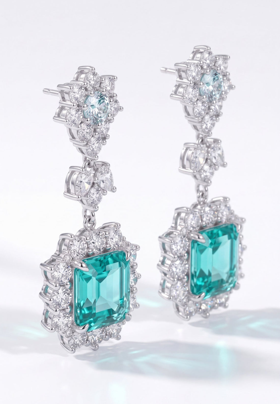 Close-up silver drop earrings with teal emerald-cut center stones and crystals