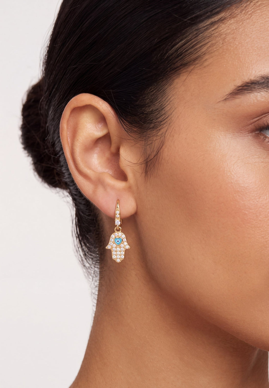 Gold hamsa drop earrings on model, blue eye center with clear stones