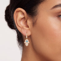 Gold hamsa drop earrings on model, blue eye center with clear stones