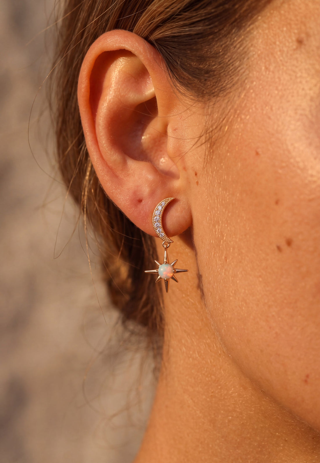 Gold crescent moon and white opal starburst drop earrings on ear with hinged backing
