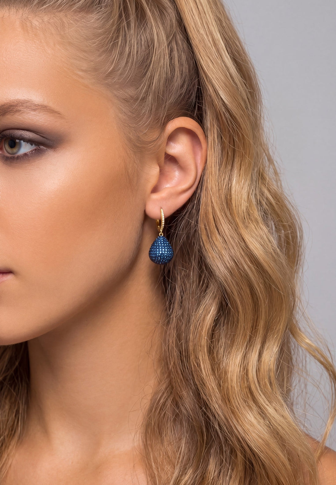 Pear drop sapphire blue gemstone earring with gold hook on model ear