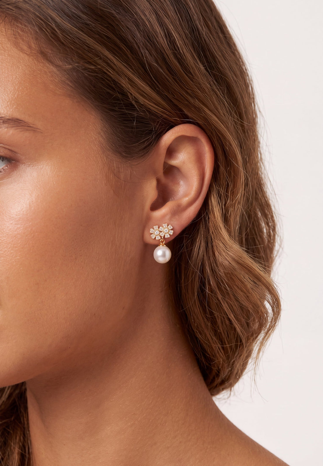 Gold-tone pearl drop earrings with crystal flower tops, worn on ear