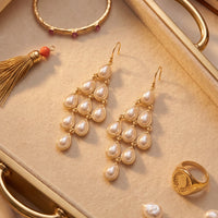 Gold-tone pearl chandelier earrings with teardrop pearls, close-up on jewelry tray