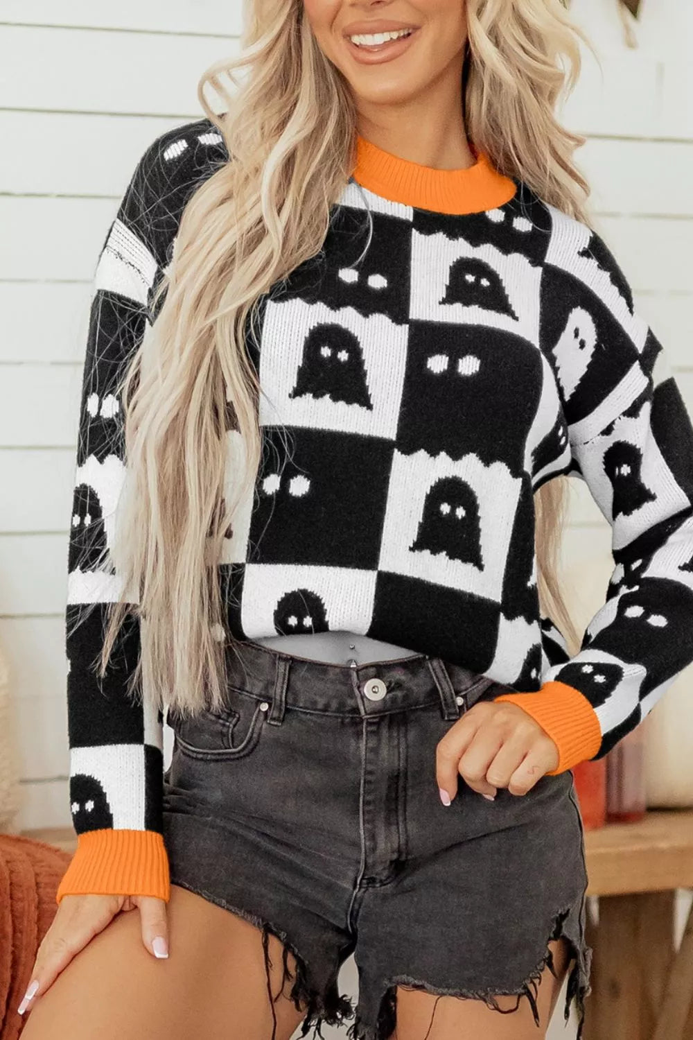 Black and white ghost checkerboard sweater with orange crew neck, cuffs, and hem