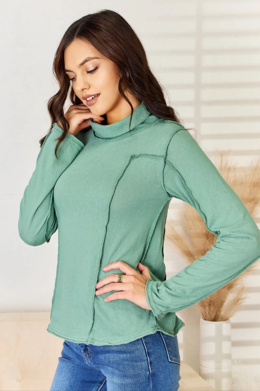 Emerald green long sleeve knit top with mock neck and curved exposed seam