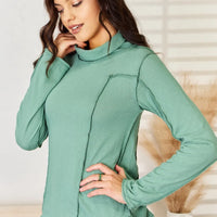 Emerald green long sleeve knit top with mock neck and curved exposed seam