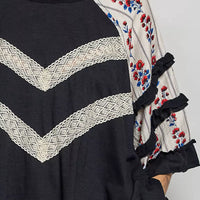 Close-up of black knit top with chevron lace detail and floral ruffle trim on sleeve