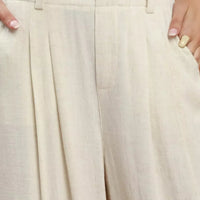 Cream trousers close-up: pleated front, waistband, and belt loops