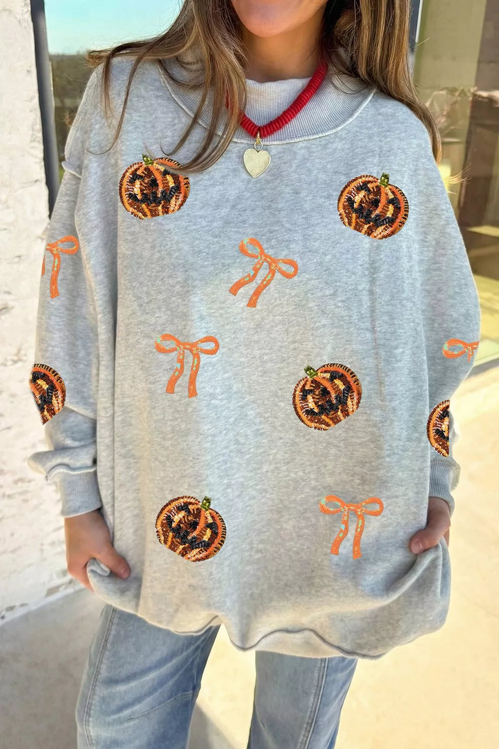 Light gray Halloween sweatshirt with orange pumpkin face and bow sequin motifs