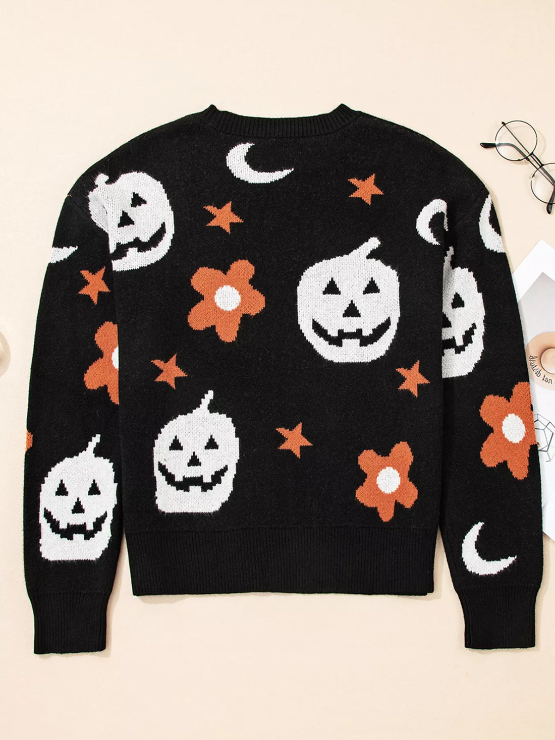 Black long-sleeve crewneck sweater with Halloween jack-o-lanterns, moons, stars, and orange blooms