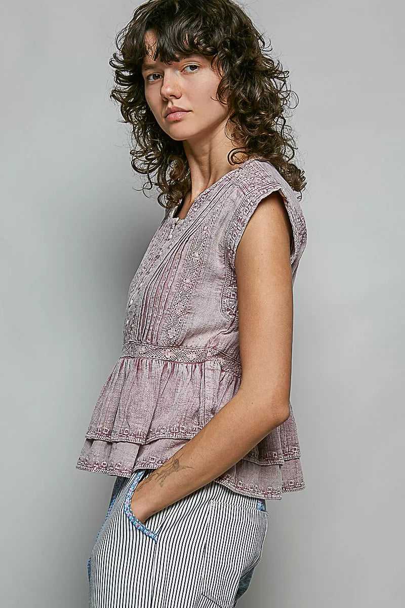 Pink sleeveless embroidered peplum blouse with button placket and layered ruffle hem.