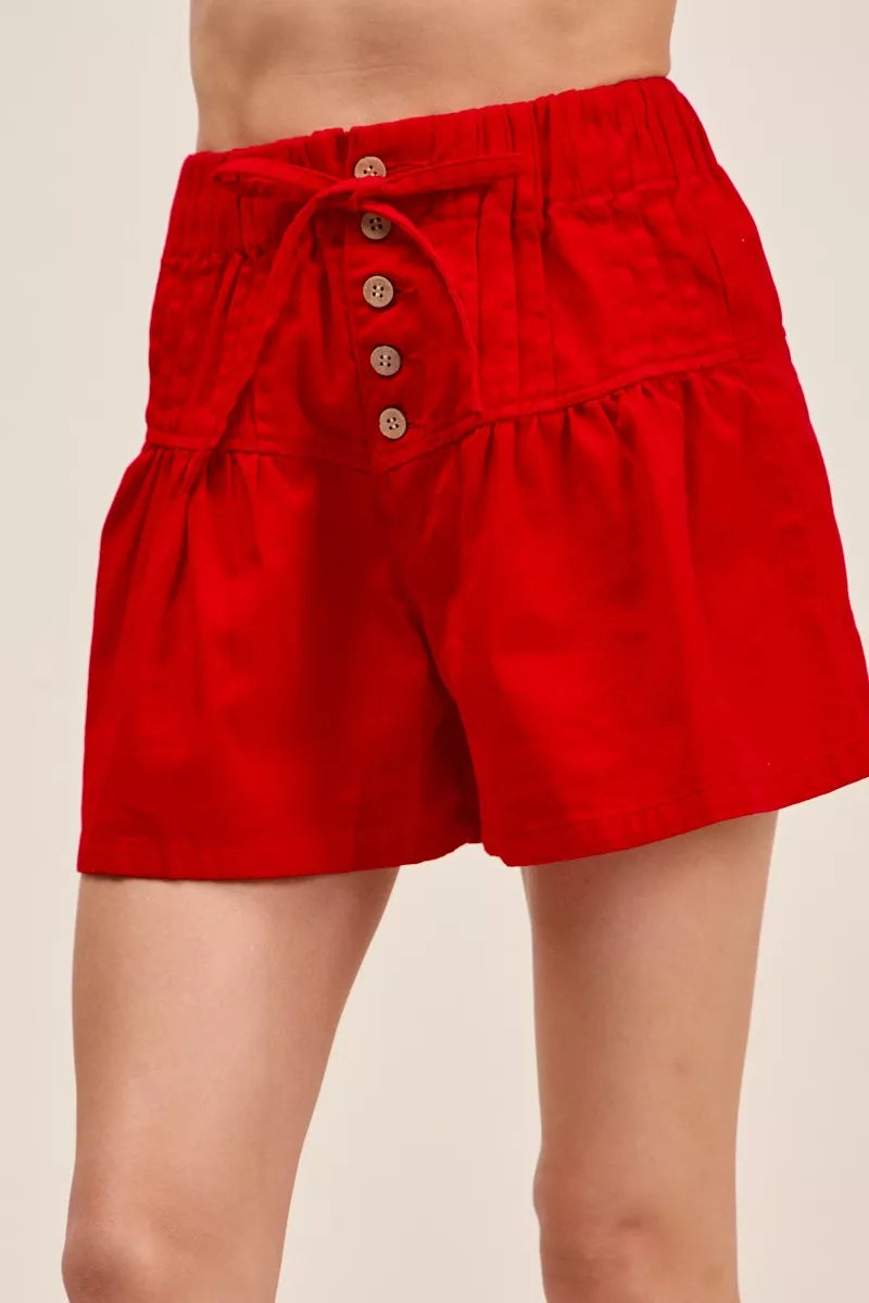 Red twill denim shorts with pintucks, button front, and waist tie; elastic waistband.