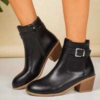 Point-toe block heel boots in black with side zipper, buckle strap, and brown sole