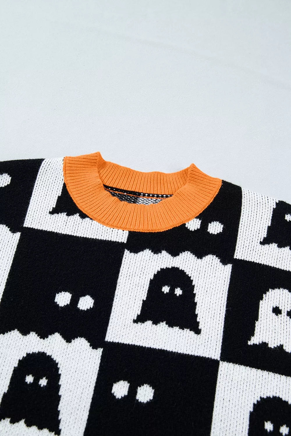 Close-up of black and white ghost checkerboard knit with orange ribbed crew collar