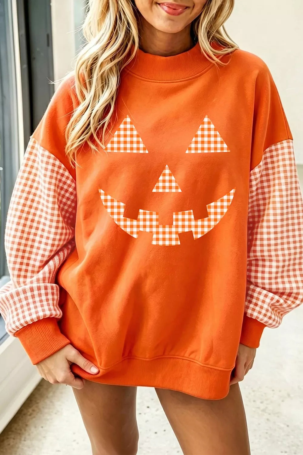 Orange pullover sweatshirt with checkered plaid sleeves and pumpkin face graphic