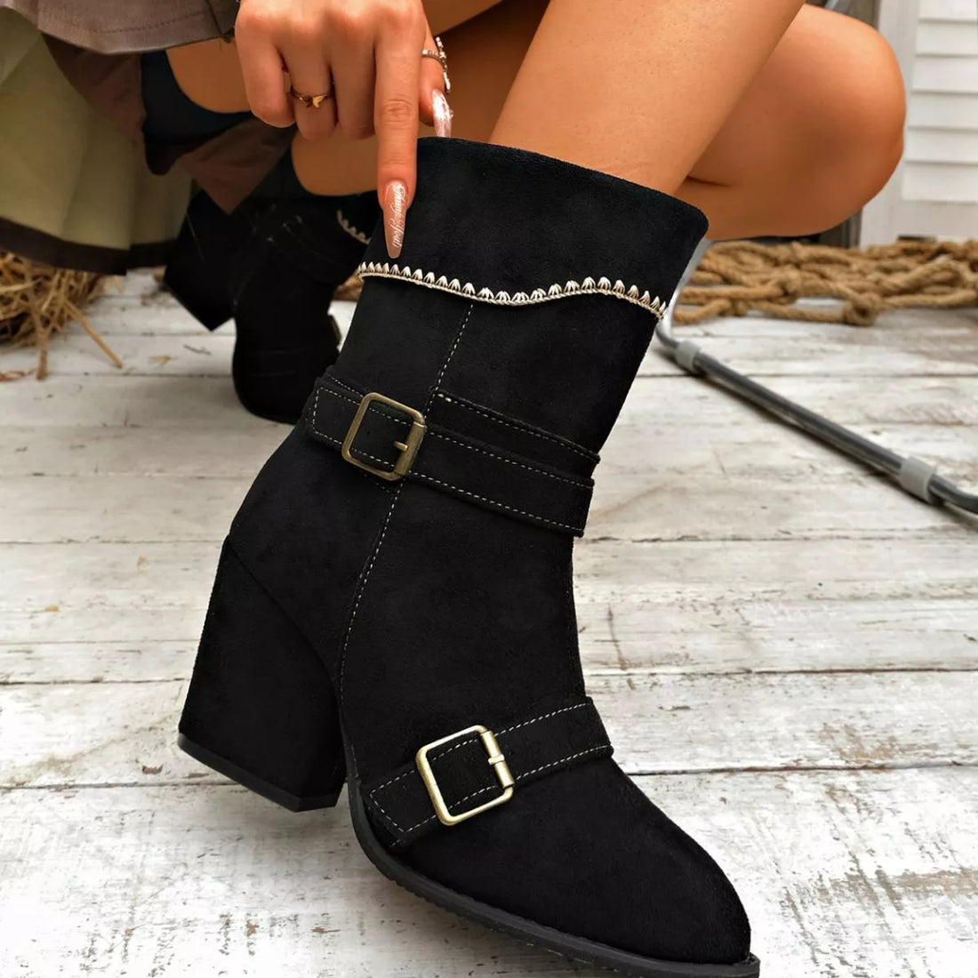 Black suede ankle boots with block heel, point toe, buckled straps and decorative trim.