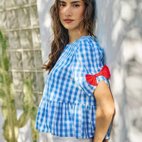Blue gingham short-sleeve blouse with red ribbon bow shoulder detail and peplum hem