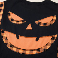 Close-up of black top with orange plaid pumpkin face applique on chest