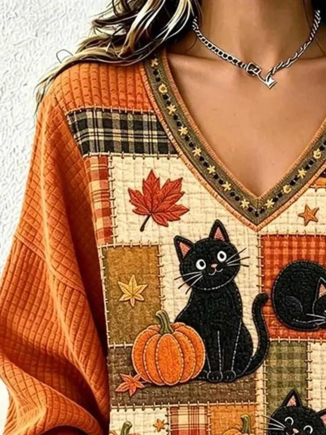 Orange V-neck sweater detail: black cat with pumpkin and leaf patchwork panel