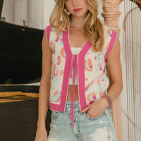 Sleeveless ivory sweater vest with pink leopard-style print, V-neck tie cords, and scalloped hem.