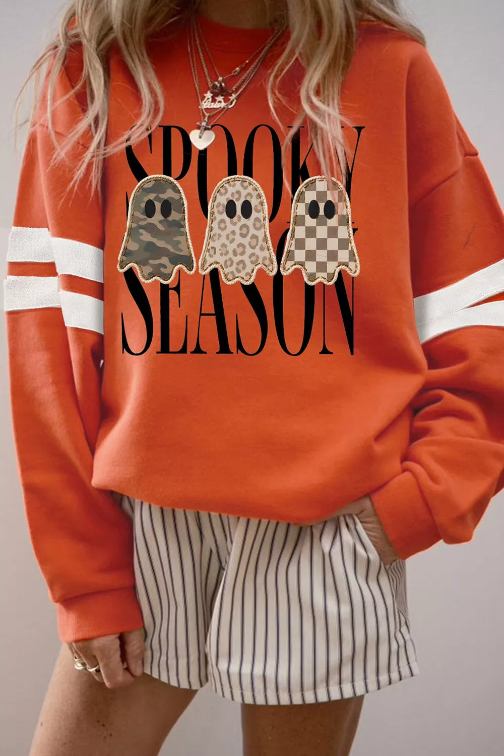Orange sweatshirt with ghost trio graphic and white striped sleeve cuffs