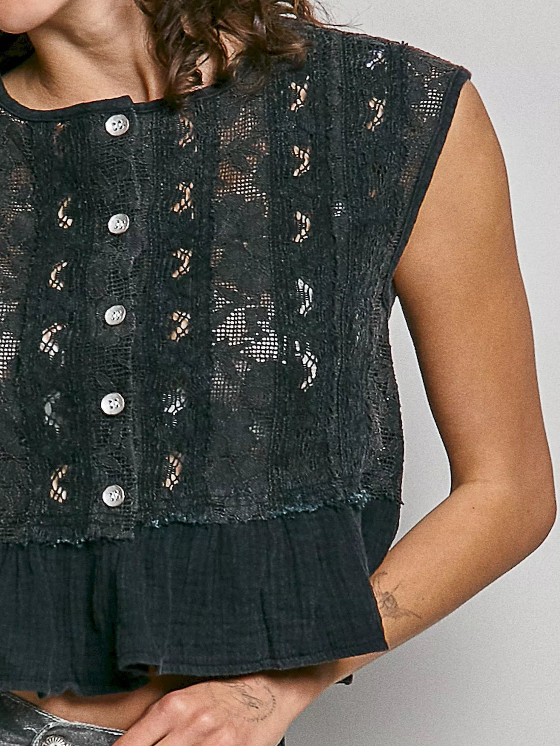 Black lace sleeveless top close-up: round neck, button placket, and ruffle hem