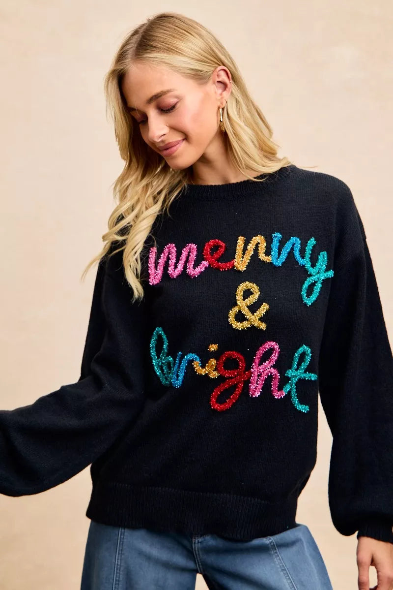 Black sweater with multicolor tinsel-style "Merry & Bright" graphic, worn with jeans
