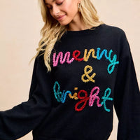 Black sweater with multicolor tinsel-style "Merry & Bright" graphic, worn with jeans