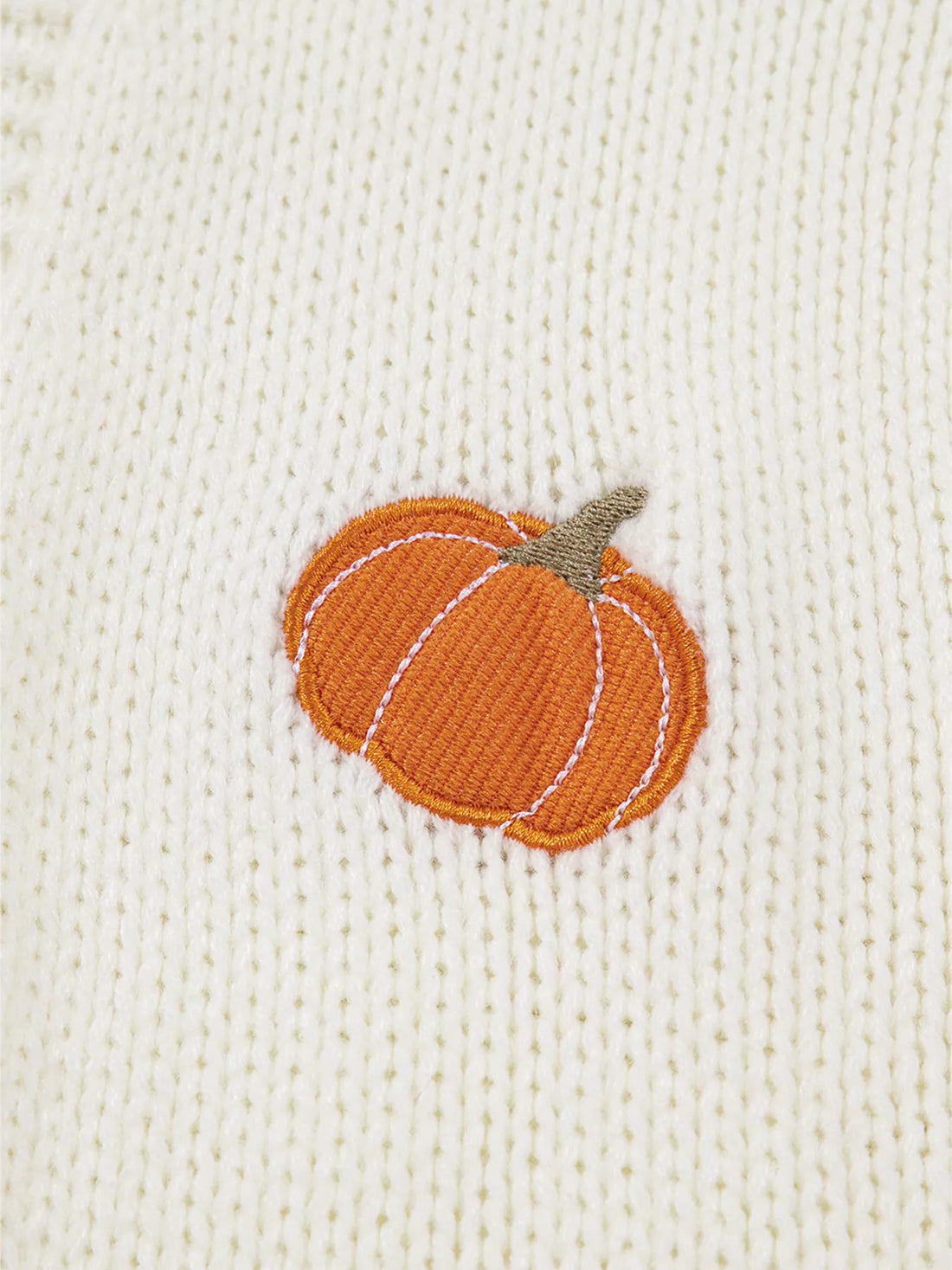 Close-up of orange pumpkin embroidery on off-white knit cardigan fabric.
