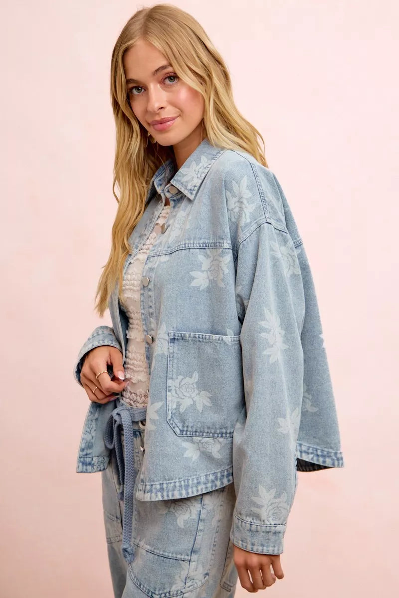 Light blue denim jacket with white floral print, button front, and chest flap pockets