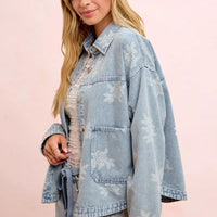 Light blue denim jacket with white floral print, button front, and chest flap pockets