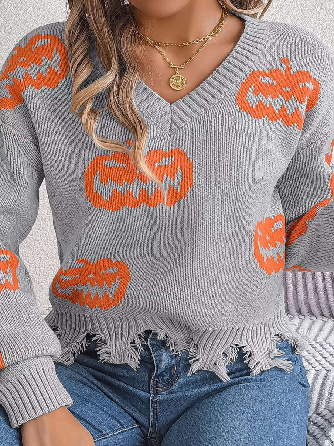 Gray knit V-neck pumpkin sweater with orange jack-o’-lanterns and frayed hem detail