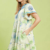 Floral babydoll dress angled view, blue contrast trim, tiered skirt on cream base