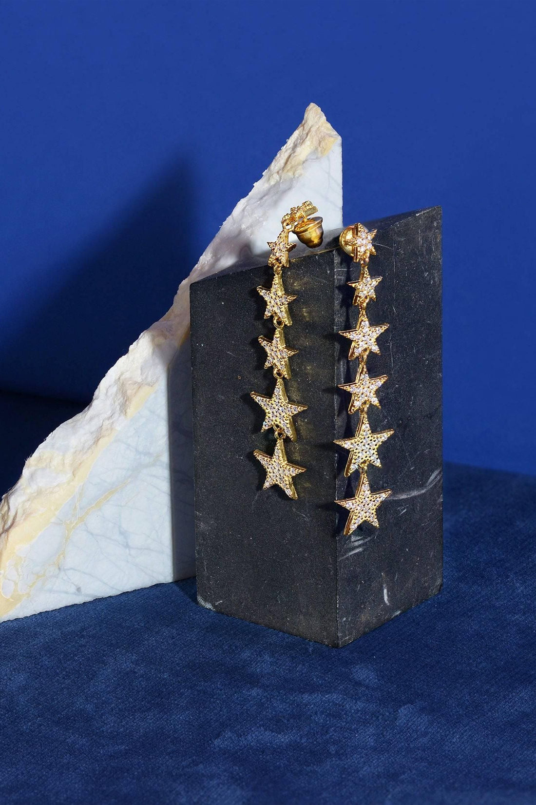 Gold star drop earrings displayed on block, five dangling star charms
